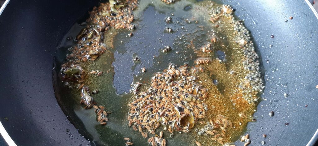 Sauting cumin and mustard seeds in a pan.